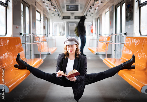 flexible female yogi reading book in the underground carriage sitting in gymnastic split. Concept of inspiration, harmony and health.