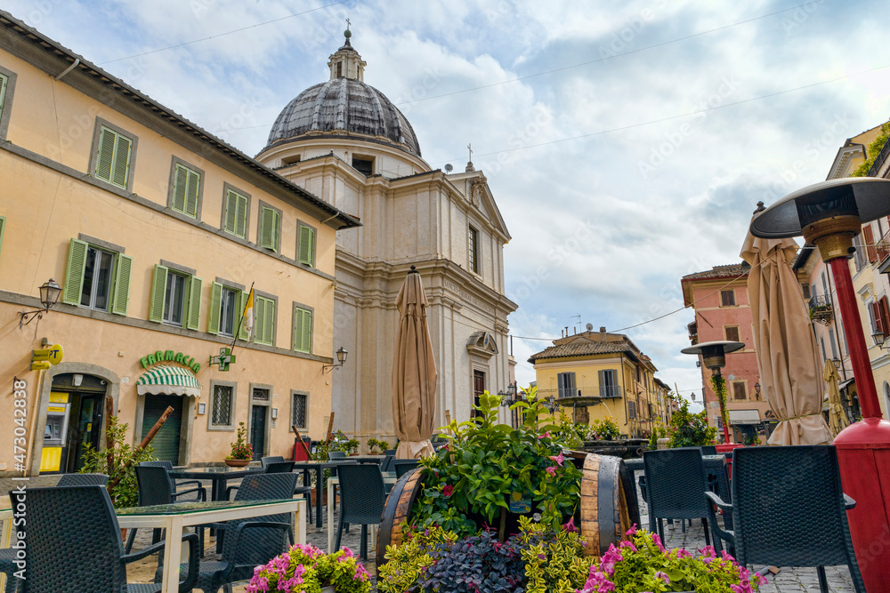 Low angle view of Castel Gandolfo downtown city street at Liberty Square with ancient buildings and Church of San Tommaso da Villanova, a famous tourist landmark in Roman Castles regional park