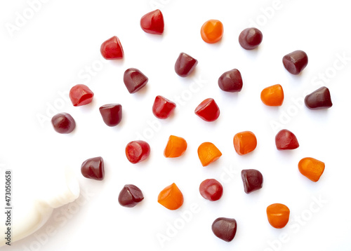 Photos Group of red, orange and purple multivitamin gummies with the bottle isolated on white background
