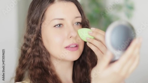 Beautiful woman applying natural organic makeup using beauty blender and smiling, eco make-up sponge tool, face portrait of caucasian model or vlogger as cosmetic product, skincare and people concept. photo