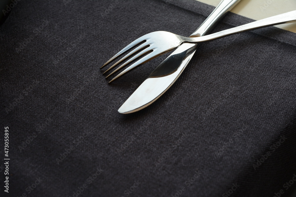 Fork and knife on a black tablecloth. Black background for your design. View from above. Stylish cutlery. Restaurant setting. Fork and knife on a black tablecloth. Black background for your design. View from above. Stylish cutlery. Restaurant setting.
