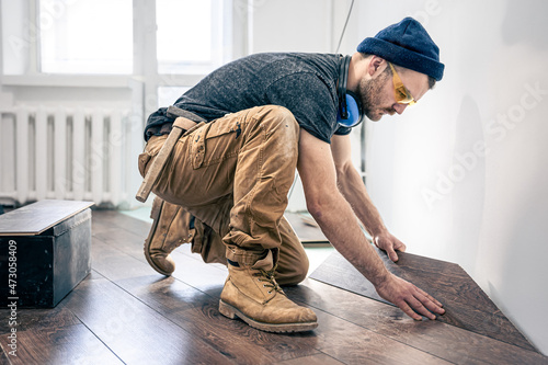 Bild auf Leinwand A male worker puts laminate flooring on the floor.