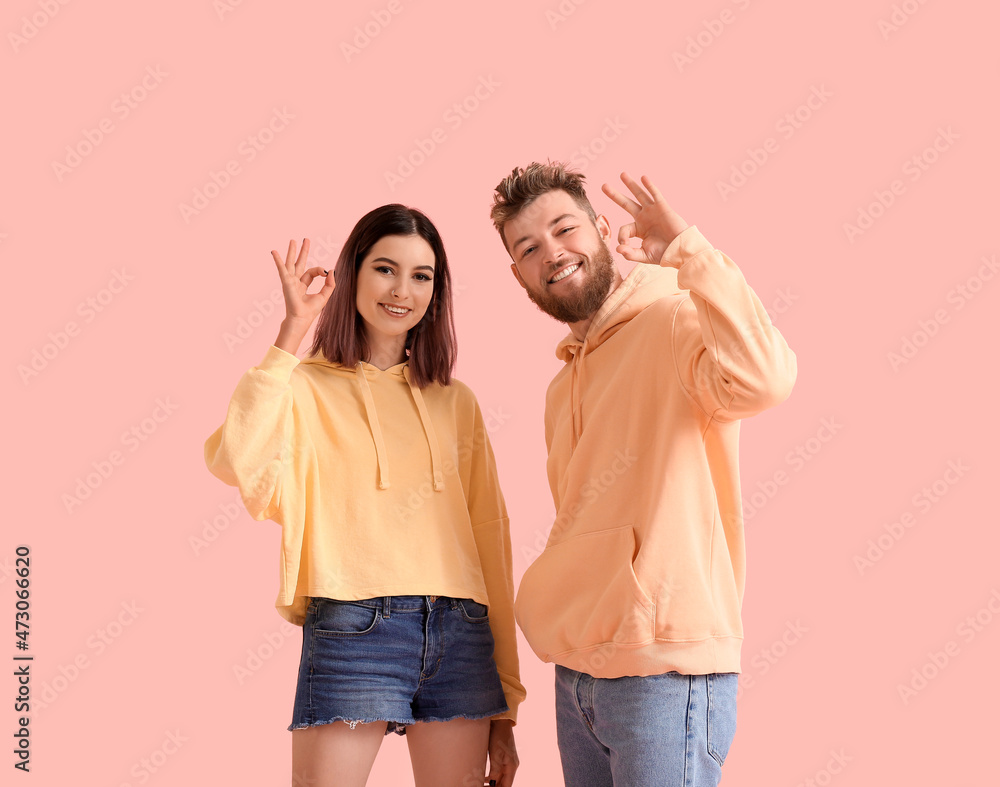Cool young couple in hoodies showing OK on color background Cool young couple in hoodies showing OK on color background