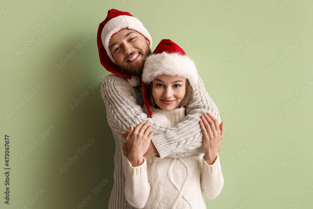 Obraz premium Happy young couple in stylish winter clothes and Santa Claus hats on color background