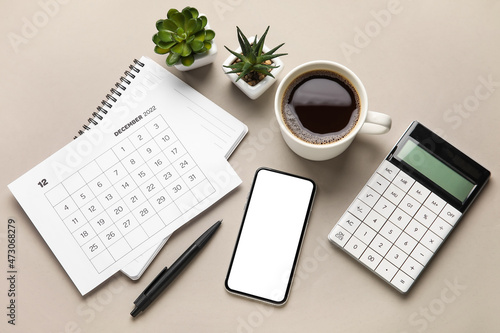 Mobile phone, paper calendar for December 2022, houseplants, cup of coffee and calculator on grey background