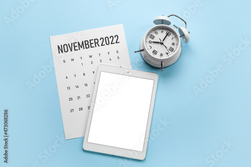 Tablet computer, paper calendar for November 2022 and alarm clock on color background
