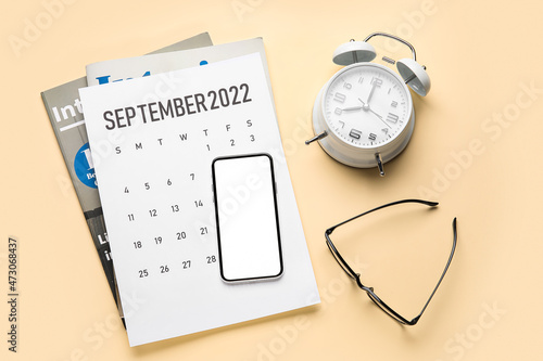 Mobile phone, paper calendar for September 2022, magazines, alarm clock and eyeglasses on color background