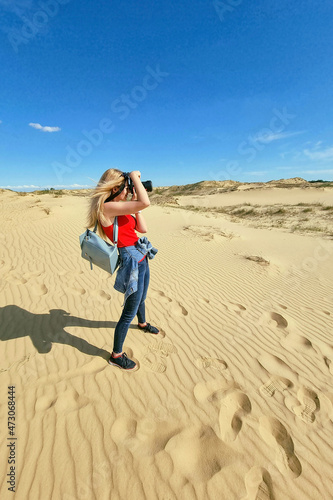 Young photographer is taking pictures in Oleshky Sand, Ukraine. Standing on the top of sand dune in desert, sand is al around and some greens. Hot summer weather, concept of travelling around planet.