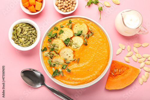 Composition with delicious pumpkin cream soup in bowl and seeds on pink background