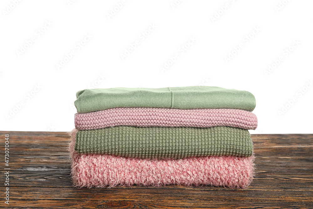 Stack of trendy sweaters on wooden table against white background Stack of trendy sweaters on wooden table against white background