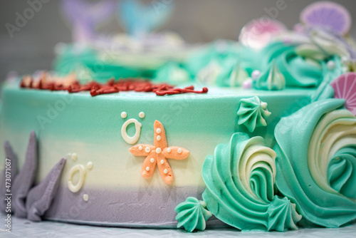 A orange starfish which is decorated on pastel colorful creamy HBD cake. Bakery and cake sweet food object photo. Selective focus.