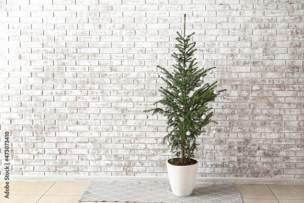 Fototapeta premium Beautiful decorated Christmas tree in pot near light brick wall