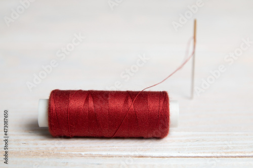 A spool of red thread and a needle on a light background.