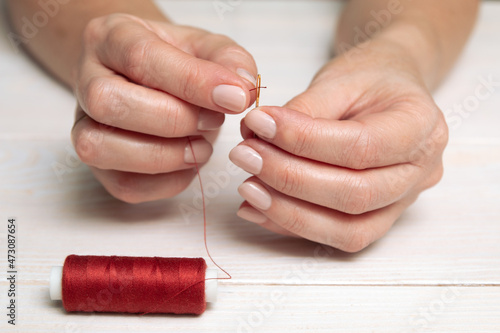 A woman inserts a red thread into a needle.
