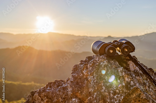 binoculars on top of rock mountain at beautiful sunset background. photo