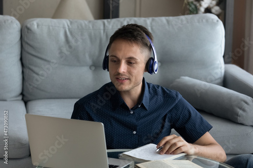 Positive student guy, intern in wireless headphones taking online business course, making video call to teacher, watching learning webinar on laptop, studying foreign language on online class photo