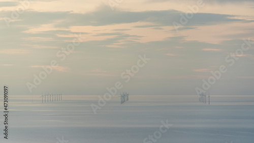 Beautiful landscape image of renewable energy wind turbine farm off North coast of Wales with lovely pastel sunset colours