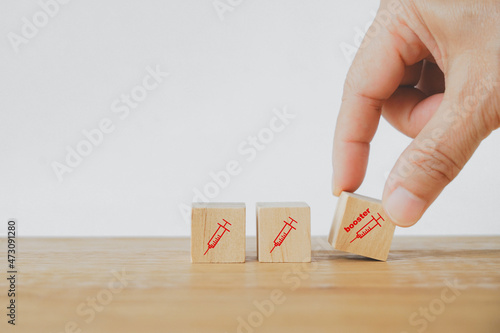 senior's hand holding booster dose vaccine text and icon on wooden cube on desk due to spread of corona virus, population, social or herd immunity concept