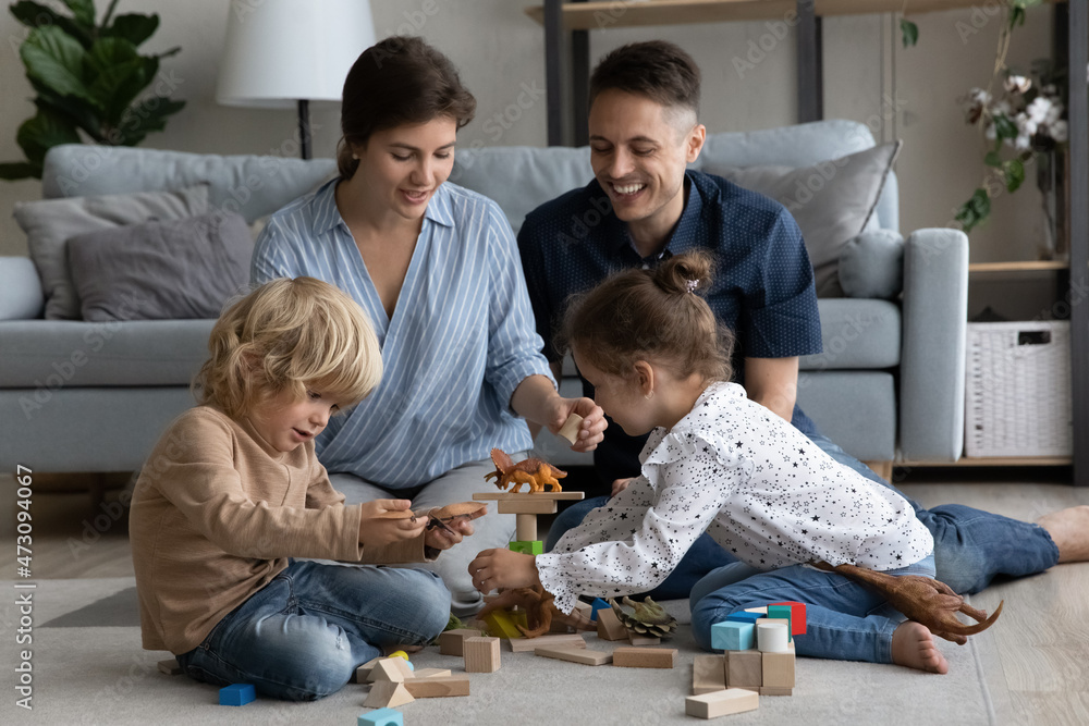 Happy mom, dad and little siblings playing with toys together on heating floor, building tower from wooden construction toys, improving kids skills in learning game, enjoying family leisure time
