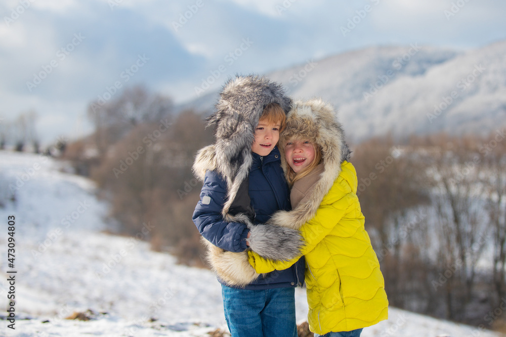 Funny little children hugging in winter outdoor. Smiling kids friends in frost snowy day outdoor. Two kids boys an girl together in park with snow background. Hapy kids emotions.