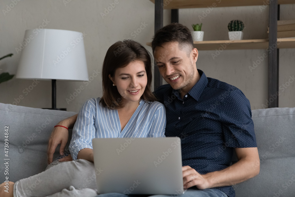 Smiling sweet relaxed married couple using ecommerce app for online shopping, making order, hugging, watching movie on internet, enjoying leisure time together on comfortable couch in living room Smiling sweet relaxed married couple using ecommerce app for online shopping, making order, hugging, watching movie on internet, enjoying leisure time together on comfortable couch in living room