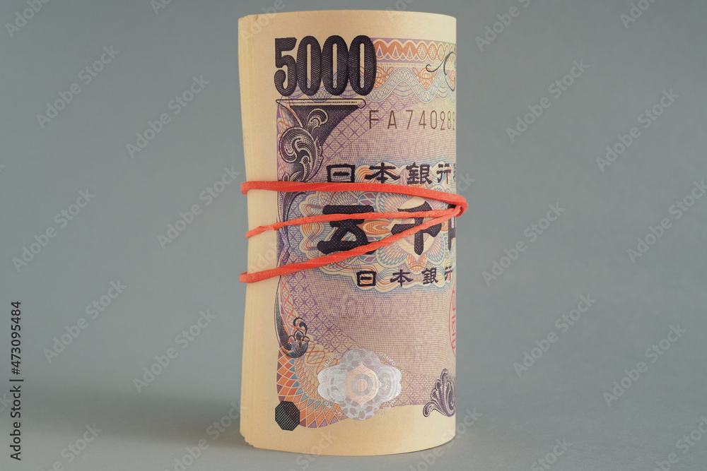 There is a bundle of 5,000 yen Japanese bills close-up. Dark gray backdrop. The banknotes are rolled up and tied with an elastic band. Deposit or loan in the bank. Macro There is a bundle of 5,000 yen Japanese bills close-up. Dark gray backdrop. The banknotes are rolled up and tied with an elastic band. Deposit or loan in the bank. Macro