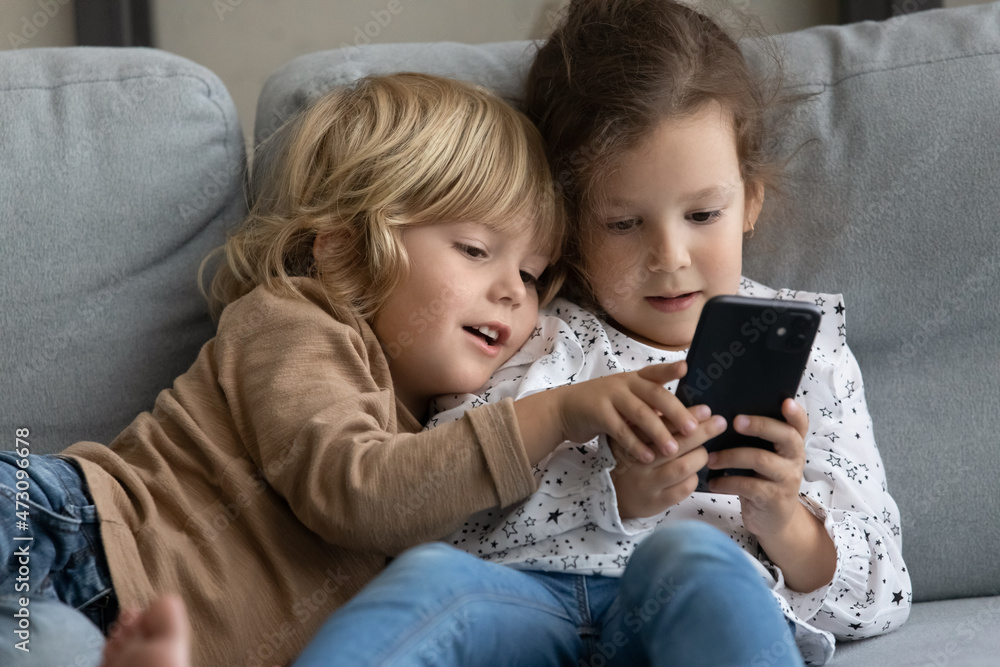 Two little toddler preschooler sibling gen Z kids using online parental control app on mobile phone, playing video game for children, sharing digital gadget, relaxing on comfortable couch at home Two little toddler preschooler sibling gen Z kids using online parental control app on mobile phone, playing video game for children, sharing digital gadget, relaxing on comfortable couch at home