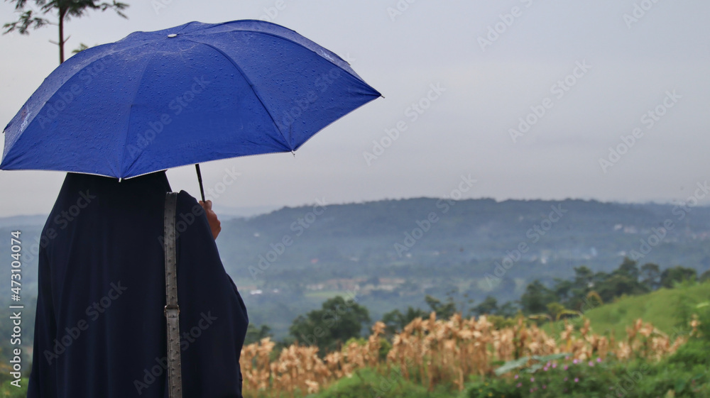 Adult women in hijabs use umbrellas while traveling in rainy nature