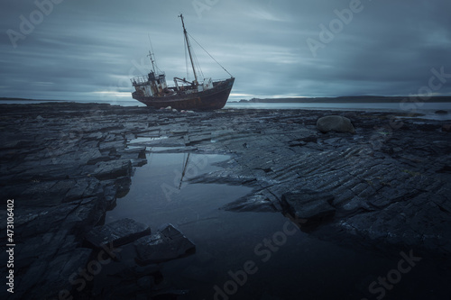 Dark blue marine natural background. Broken bot lies on its side, thrown on the rocks. Cape Nenetsky. Kola Peninsula. Teriberka. Murmansk. photo
