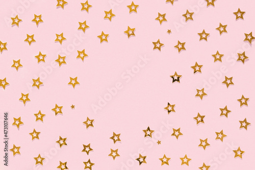 Golden stars glitter confetti on pink background with round copy space. Gold sparkles texture. Holiday new year backdrop. Anniversary, birthday. Greeting card template. Sale, event star pattern
