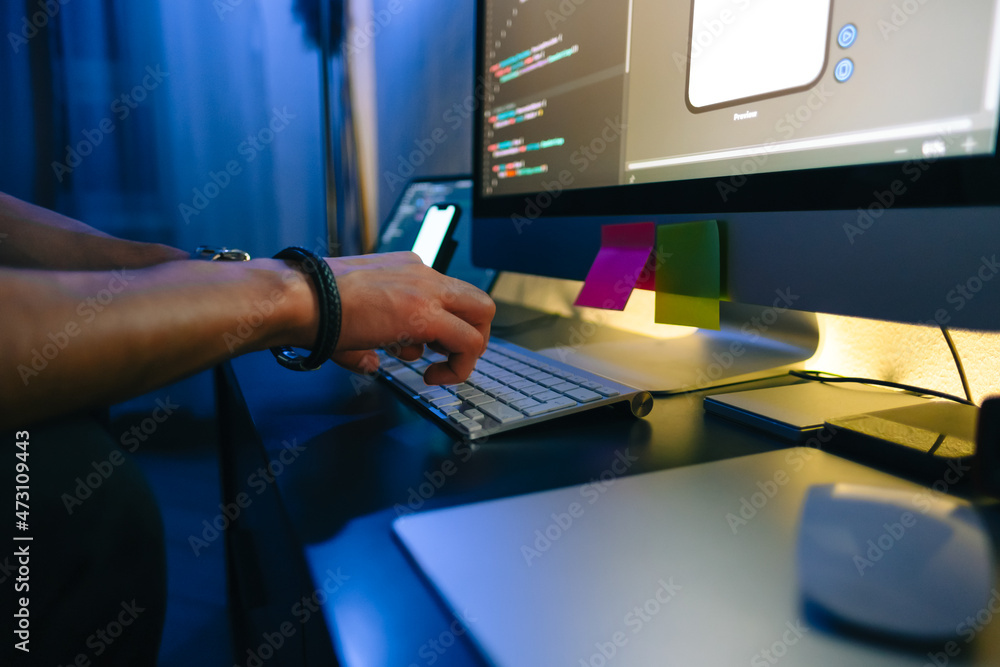 Naklejka premium Mobile developer writes program code on a computer, typing on keyboard, programmer work in home office.