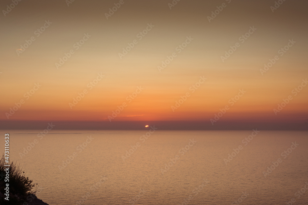Sun at horizon disappearing behind the clouds as it sets over the sea in Zakynthos island, Greece