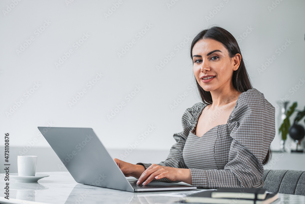 Smiling businesswoman typing on laptop and notebook on desk, office room Smiling businesswoman typing on laptop and notebook on desk, office room