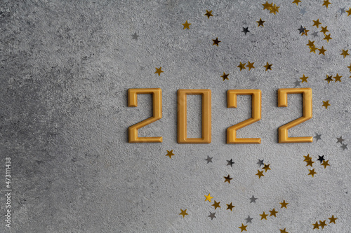 Happy new year 2022. Gold numbers with golden Christmas decoration stars on dark grey background. Holiday greeting card design. New year festive concept. Top view copy space.