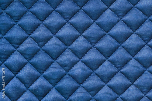 Quilted fabric. Background blue cloth sewn into the cell, stitching. Texture of the blanket, blue textile