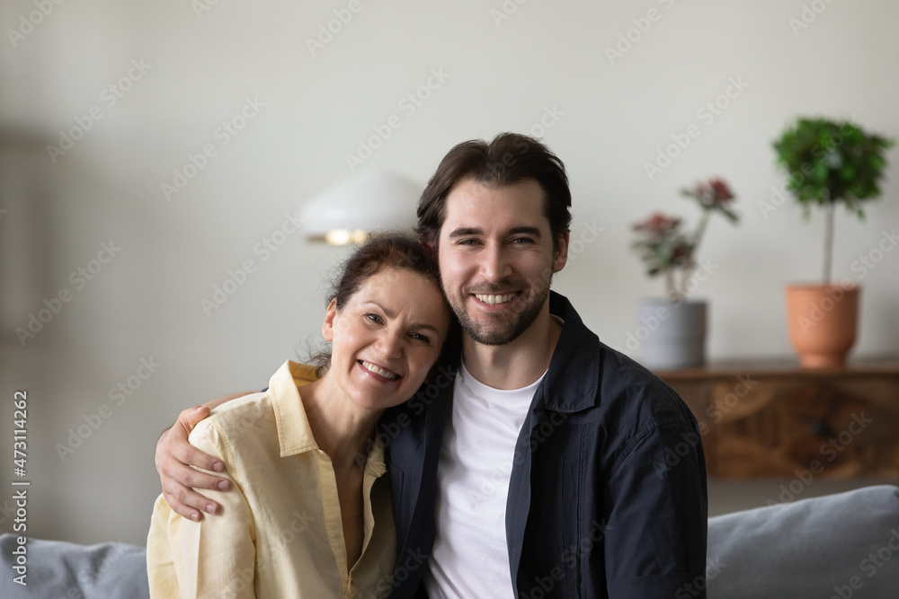 Happy grown son and senior mother meeting, enjoying leisure time together, having fun at home, sitting on couch, hugging, looking at camera. Motherhood, family concept. Head shot portrait Happy grown son and senior mother meeting, enjoying leisure time together, having fun at home, sitting on couch, hugging, looking at camera. Motherhood, family concept. Head shot portrait
