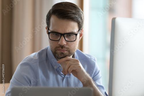 Photography Focused business professional man in glasses working on project at two monitors