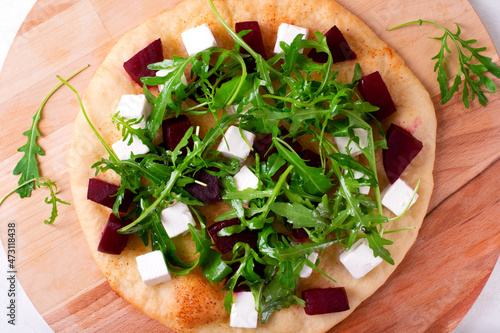 Pizza with roasted beet, feta cheese and arugula on the wooden board. Top view
