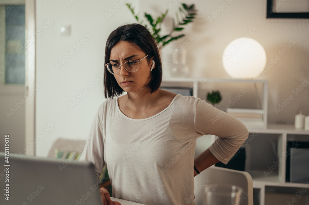 Beautiful woman having back and neck pain while using a laptop at home Beautiful woman having back and neck pain while using a laptop at home