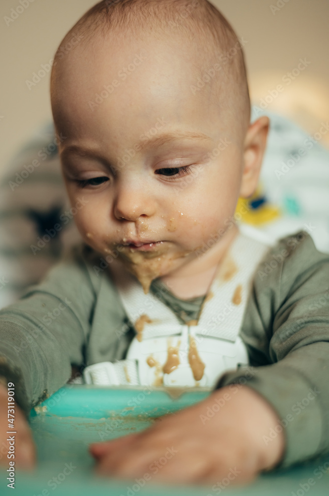Baby eating with a face stained in food while in a child's dining chair Baby eating with a face stained in food while in a child's dining chair