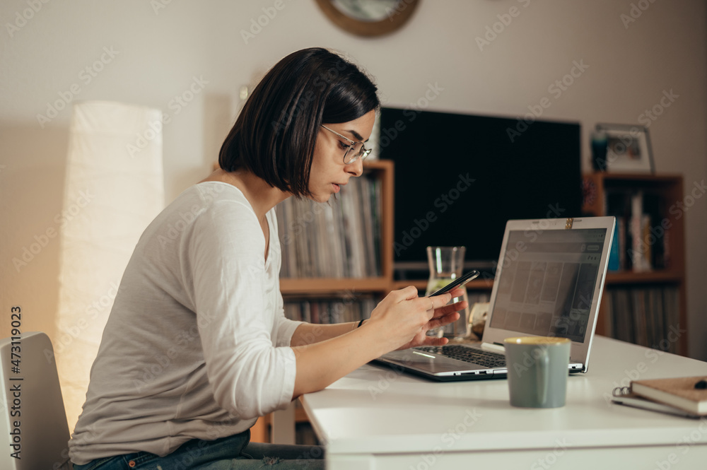 Beautiful woman using smartphone and a laptop while working from home
