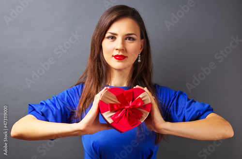Beautiful girl holding gift in heart form on gray background © es0lex