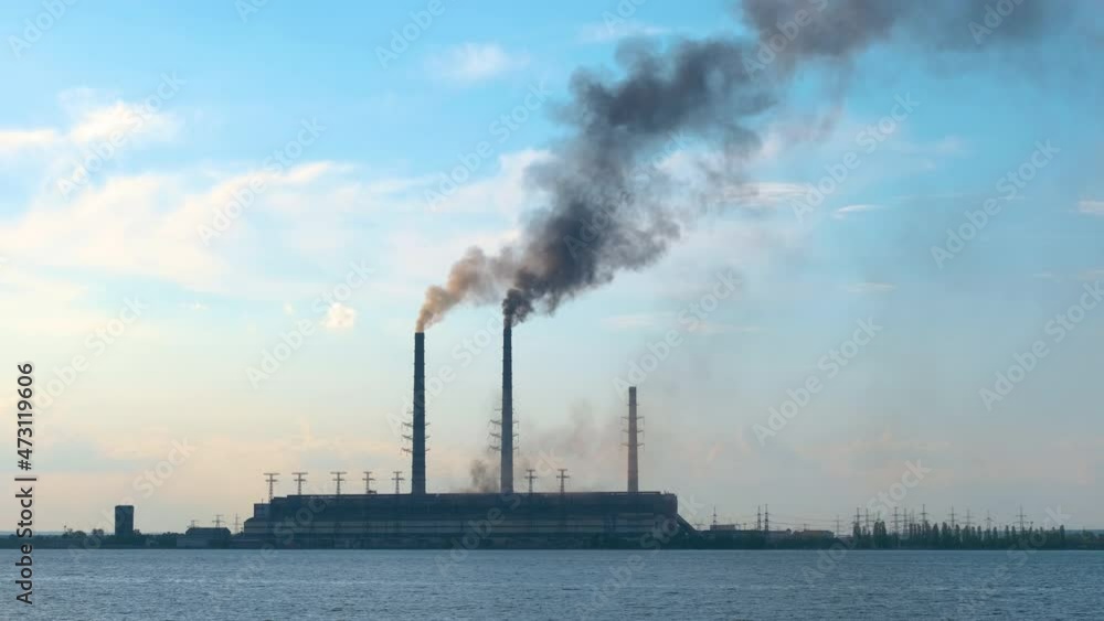 Coal power plant high pipes with black smoke moving upwards polluting atmosphere over lake water