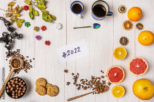 Still life top view with assortment of citrus fruits, chocolate bonbons, paper stars, coffee cups, chocolate cookies and wooden table and the new year 2022