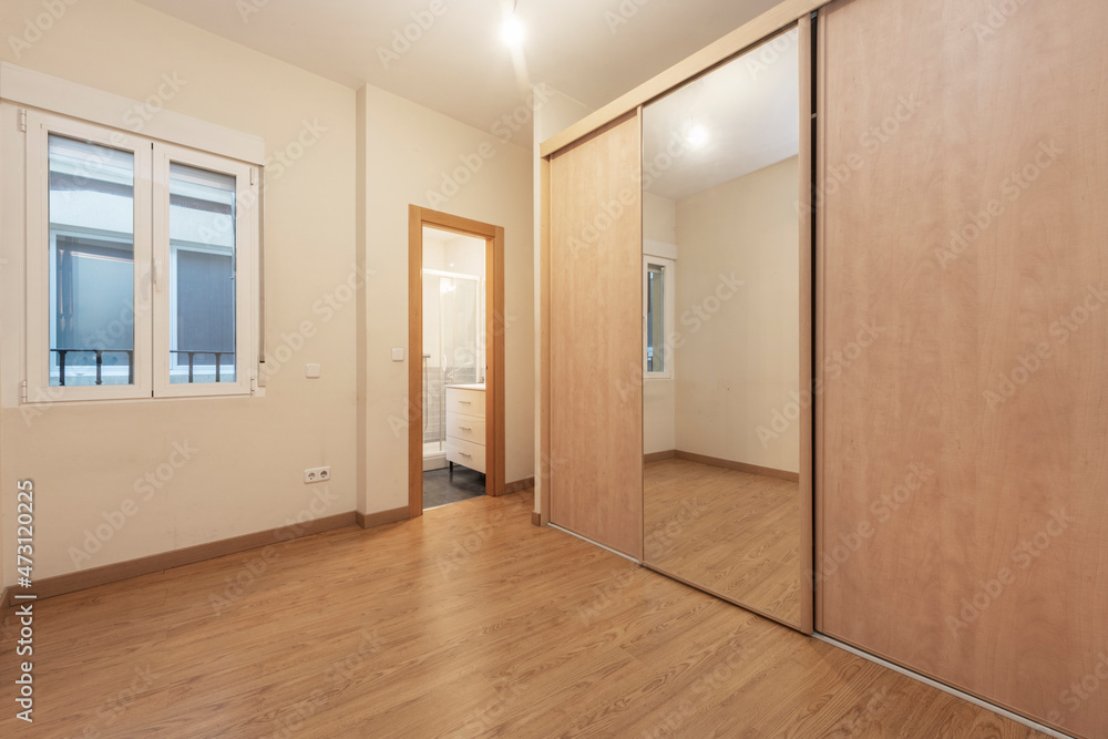 Empty furniture room with built-in wardrobe with large mirror door and separate toilet and view of hallway Empty furniture room with built-in wardrobe with large mirror door and separate toilet and view of hallway