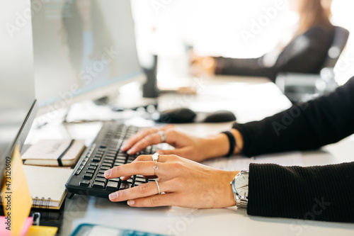 Close up of woman's hands typing a computer on a messy desk