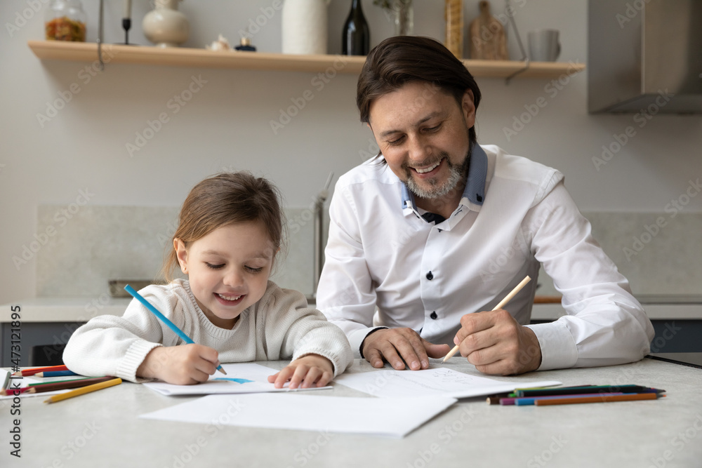 Happy cute little preschool kid daughter drawing picture with pencils, enjoying art activity with caring young 35s father, sitting together at table at home, early development, domestic pastime. Happy cute little preschool kid daughter drawing picture with pencils, enjoying art activity with caring young 35s father, sitting together at table at home, early development, domestic pastime.