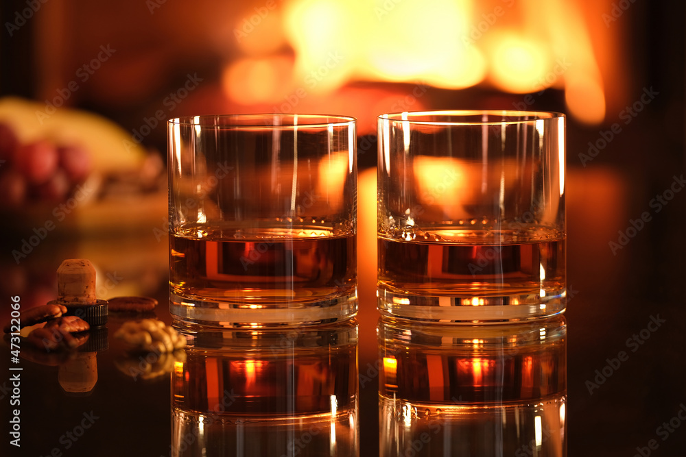 Two glasses with whiskey and serving on the fireplace background. Romantic dinner. Two glasses with whiskey and serving on the fireplace background. Romantic dinner.