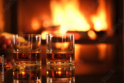 Two glasses with whiskey and serving on the fireplace background. Background with text space.