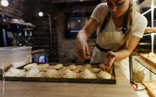 a girl cook in a cafe sprinkles coconut shavings on raw pies lying on a tray. open kitchen cooking
